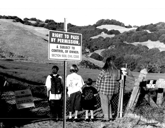 Young people, on the shoulder of Sonoma Mountain Road, look past the locked gate 